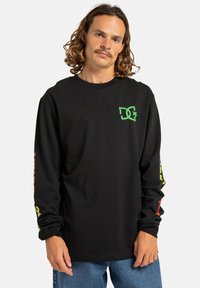 Black long-sleeve t-shirt featuring green logo on the chest and colorful text graphics running down the sleeves. Cotton material.