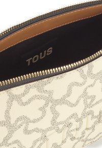 Bolso clutch de crema texturizada con un sutil patrón gris, cierre de cremallera dorado y forro interior marrón con el logo "TOUS".