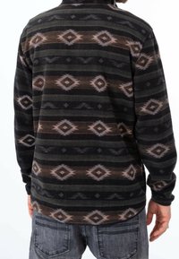 Fleecepullover med ett mönster i svart, grått och brunt, som har diamantsformer och horisontella ränder. Mjuk textur, lång ärm.