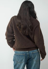 Brown, textured sweater with a relaxed fit, paired with light blue denim jeans featuring visible back pockets, displayed from behind.