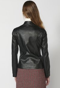 Czarna skórzana kurtka o dopasowanym kroju, z teksturowanymi akcentami na ramionach i gładkim wykończeniem, zestawiona z czerwoną i białą kratkowaną spódnicą.