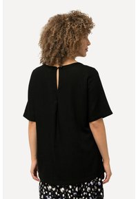 Schwarzes Leinenhemd mit rundem Ausschnitt, kurzen Ärmeln und einem Schlitzdetail auf der Rückseite. Der Saum ist abgerundet und sorgt für eine lockere Silhouette.