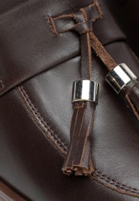 Braunes Leder-Schuhwerk mit glatter Oberfläche, Quasten-Detail und silbernen Akzenten. Die Naht entlang des Randes verleiht Textur und Design.