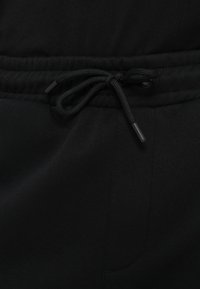 Μαύρο παντελόνι τζόγκερ με ελαστική μέση, διαθέτοντας κλείσιμο με κορδόνι και λεία υφή υφάσματος. Διακριτική ραφή στο πλάι.