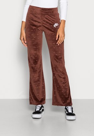 Brune velour Nike Air bukser med et subtilt logomønster, båret med sorte og hvide sneakers og en hvid langærmet top.