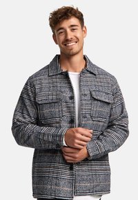 Plaid jacket in blue, gray, and beige textile with a button-up front, two chest pockets, and a collared neckline. Woven texture details visible.