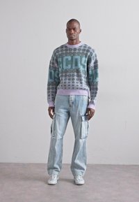 Pulover tricotat de culoare gri, cu accente în aqua și lavandă, având un model geometric. Asortat cu blugi cargo de culoare albastru deschis și adidași albi.