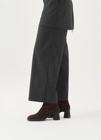 Brown suede ankle boots with a square heel, paired with wide dark gray trousers featuring raw hem details.