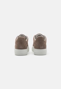 Brown suede sneakers with a white rubber sole, featuring a padded collar and tongue. Minimalist design with no visible patterns or hardware.