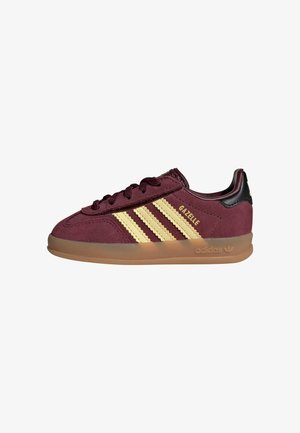 Bordowe buty sportowe Adidas Gazelle z beżowymi paskami, gumową podeszwą, czarną zakładką na pięcie i złotym napisem "GAZELLE" po boku.