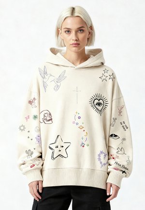 Jonge vrouw met kort blond haar, gekleed in een crème kleurige hoodie versierd met kleurrijke, handgetekende schetsen en symbolen.