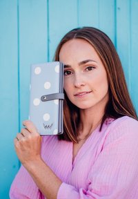 Light blue wallet featuring large white polka dots, a gray strap, and silver hardware. Smooth texture with a sleek design.