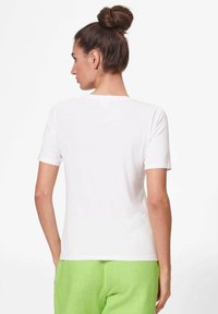 White t-shirt with short sleeves and a round neckline, paired with bright green pants. Smooth fabric texture, simple design, rear view.