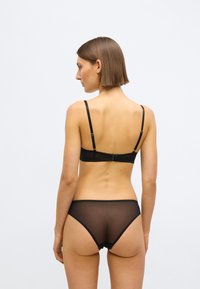 Čierna sieťovaná súprava spodnej bielizne obsahujúca braletku s tenkými ramienkami a zodpovedajúce nohavičky typu cheeky s vlnitými okrajmi a minimálnymi hardvérovými detailmi.