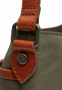 Borsa di stoffa verde con una tracolla in pelle marrone, dotata di un gancio metallico e di un bottone con logo. Texture liscia con cuciture a contrasto.