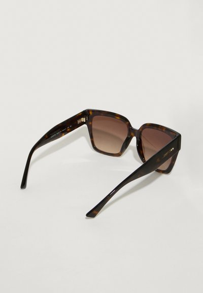 Lunettes de soleil en écaille brune avec des montures angulaires, des verres dégradés et des branches fines. Présente une gravure du logo sur le côté.