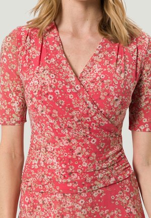 Bloemen wikkeljurk met een roze basis en kleine witte en gele bloemen. Korte mouwen en plooidetails op de taille. Zachte stoftextuur.