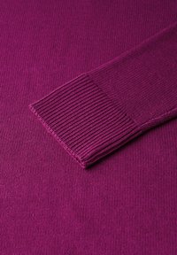 Un pull fuchsia vibrant avec des poignets en côte doux et un corps lisse et texturé. Un gros plan montre des motifs de tricot complexes.