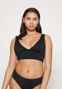 Conjunto de bikini preto com topo cropped de decote em V e alças largas, e parte de baixo de corte baixo, feito de um tecido suave e elástico.