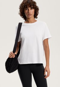Hvid bomulds T-shirt med en afslappet pasform, korte ærmer, kombineret med højtaljede sorte leggings og en struktureret sort taske.