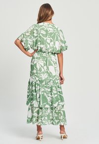 Vestido maxi de estampado verde y blanco con diseño en capas, cintura elástica, mangas acampanadas y un corte relajado. Textura de tela suave.