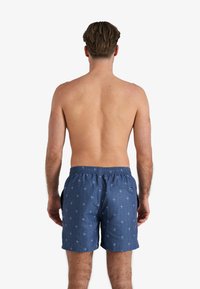 Blauwe zwembroek met een palmbomenpatroon, elastische taille en zakken, getoond van achteren op een bloot torso. Gemaakt van een katoenmix.