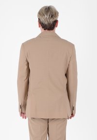 Giacca su misura color marrone chiaro con singolo spacco, due bottoni e colletto a punta, caratterizzata da un tessuto liscio e tasche aggiuntive.