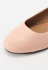Lys rosa skinnballet flats med rund tå, myk tekstur og minimalt design. Svart såle som komplementerer overdelen.