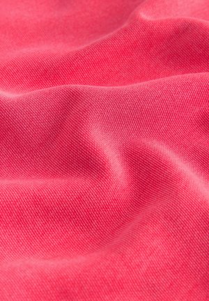 Tuvplāns mīkstai, krokaina rozā auduma virsmai ar smalku tekstūru un pinumu, kur gaisma un ēnas akcentē krokas.