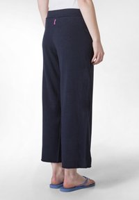 Marineblauwe wijde broek gemaakt van zachte stof met een gladde textuur. Heeft een tailleband en een klein roze label aan de achterkant.