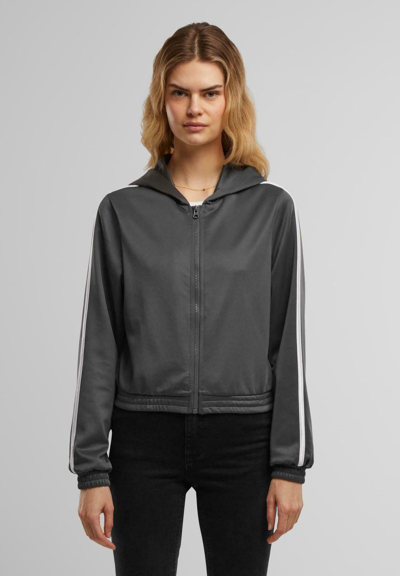 Giacca zip-up grigia con cappuccio, caratterizzata da strisce bianche a contrasto lungo le maniche e polsini elasticizzati. Tessuto liscio e leggero.