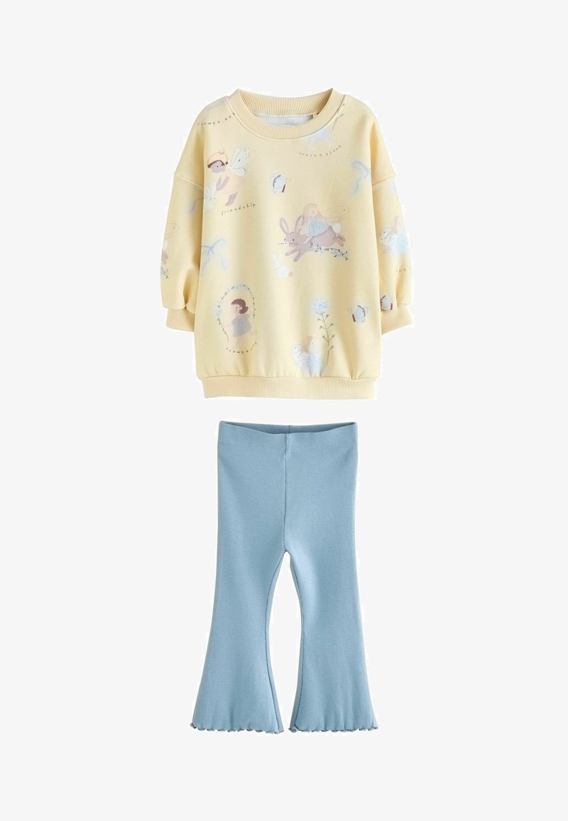 Sweat-shirt jaune avec des illustrations ludiques et des poignets côtelés, associé à des leggings évasés bleu clair en tissu à texture lisse.