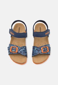 Infradito blu scuro con accenti arancioni. Presentano una fascia decorata con una fibbia e un plantare in sughero. Chiusura regolabile in velcro. Marchio Geox visibile.