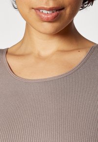 Light brown ribbed top with a round neckline, featuring a soft texture and subtle sheen, visible against skin tone in close-up view.