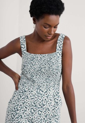 Blomstret kjole med firkantet halsudskæring, smocket bodice og brede stropper. Har et mønster af hvide tusindfryd på en mørkegrøn baggrund.
