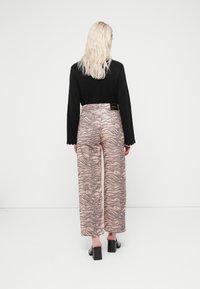 Black long-sleeve top paired with pink wide-leg pants featuring a zebra pattern. The model wears block-heeled black shoes.