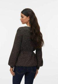 Brązowy, teksturowany kardigan z paskiem i długimi, obszernymi rękawami, z szerokim kołnierzem, noszony na ciemnych jeansach.