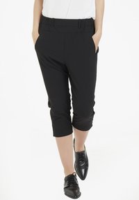 Pantalones cropped negros con una textura suave, que presentan una cinturilla estructurada y bolsillos laterales, combinados con zapatos negros de cordones.