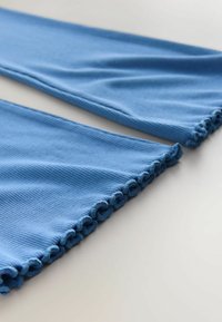 Tela azul acanalada con un acabado texturizado. El dobladillo presenta un diseño fruncido con volante, que muestra un borde liso y redondeado.