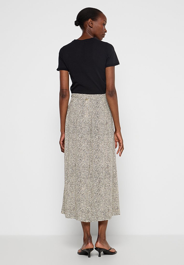 Czarny t-shirt z krótkim rękawem w połączeniu z zwiewną, wzorzystą spódnicą midi w odcieniach beżu i czerni. Gładka faktura, proste zapięcie na guziki w talii.