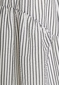 Tecido branco com riscas verticais pretas, apresentando uma aparência texturizada e ligeiramente enrugada. Os padrões criam um interesse visual subtil.