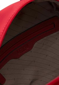 Interno di una borsa in tessuto rosso con una fodera marrone caratterizzata da sottili strisce verticali. Include una tasca con zip e dettagli di branding.