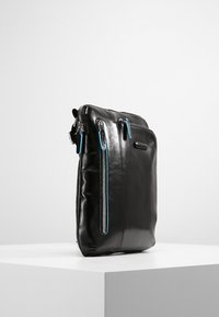 Bolso de hombro de cuero negro con dos bolsillos con cremallera azules, diseño elegante, forma rectangular y textura suave. Incluye correa ajustable.