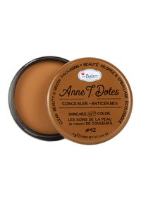 Cirkulär kosmetikbehållare med en glansig svart kant och ett brunt lock, med text och en beige concealer inuti. Storlek: 9g.