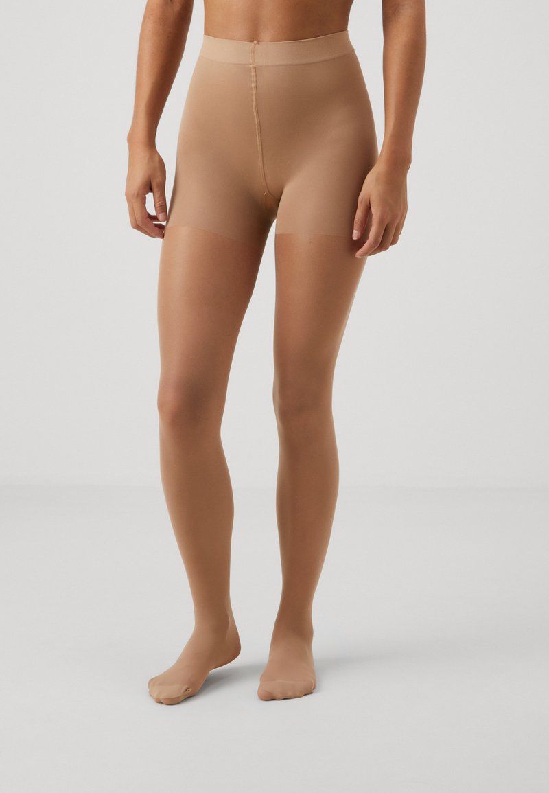 Beige transparente strømpebukser med høj talje, glat tekstur og lukkede tæer. Designet til at give et tætsiddende udseende på benene.