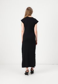 Svart maxikjole med korte cap-sleeves, smal passform og sidesplitter. Glatt stoff og minimalistisk design, parret med svarte høyhælte sandaler.
