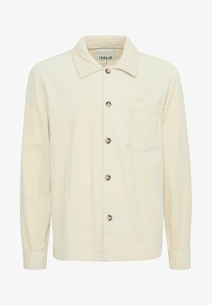 Bezs színű kordbársony ingdzseki, gombos elülső résszel, hegyes gallérral, egyetlen mellzsebbel és textúrált anyaggal. Fából készült gombokkal rendelkezik.