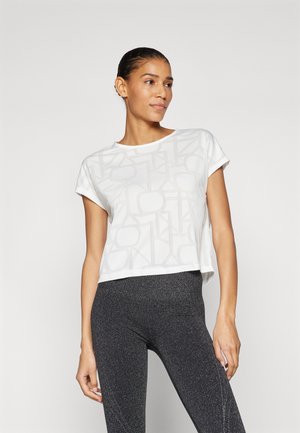 Weißes kurzärmliges Crop-Top mit einem strukturierten geometrischen Muster. Kombiniert mit dunklen, glitzernden Leggings. Schlichtes, zeitgemäßes Design.