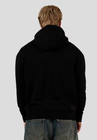 Sudadera negra con una capucha grande, pu�ños y dobladillo acanalados. Textura de tela suave; combinada con jeans de mezclilla de lavado claro.