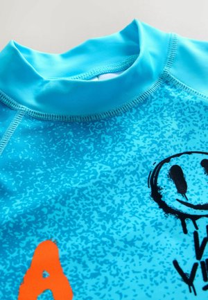 Kirkkaan sininen patojensuoja, jossa on sileä pinta, lyhyt korkea kaulus ja mustia sekä oransseja graafisia kuvioita.